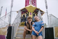 two young people sitting on the steps of a carnival ride, posing for a photo