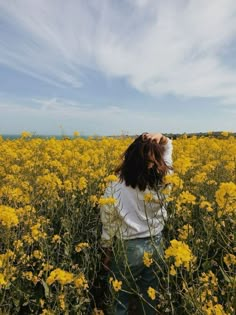 a woman standing in a field of yellow flowers with her hair blowing in the wind