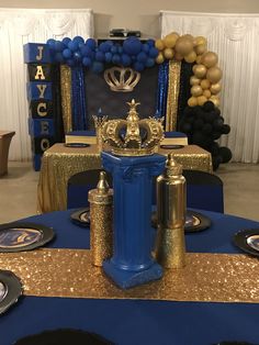 a blue table topped with a trophy next to black plates and silverware on top of a blue table cloth covered in gold sequins