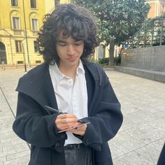 a young man is standing on the street looking at his cell phone and writing something