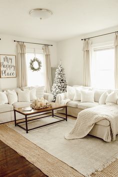 a living room filled with white furniture and a christmas tree in the window sill