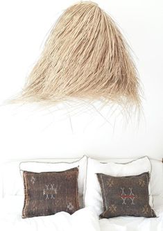 a white bed topped with two pillows and a hair hanging from the wall above it