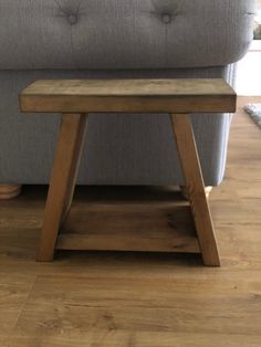 a wooden stool sitting on top of a hard wood floor next to a gray couch