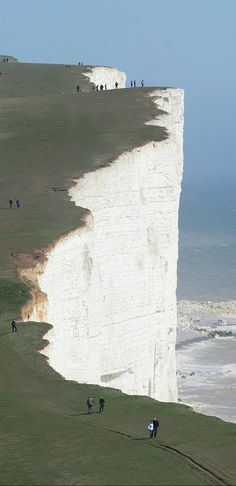 people are standing on the edge of a cliff overlooking the ocean with a lighthouse in the distance