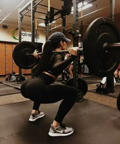 a woman squats down while holding a barbell in a crossfit gym