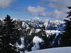 the mountains are covered with snow and trees in the foreground, under a partly cloudy sky