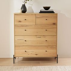 a wooden dresser with two black vases on top and a white wall behind it