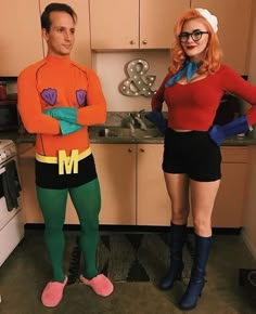 two people dressed up in costumes standing next to each other near an oven and stove top