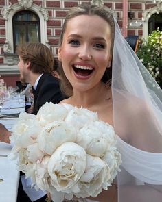 a woman in a wedding dress holding a bouquet of white flowers and smiling at the camera