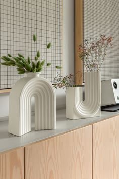 two white vases sitting on top of a counter next to a computer keyboard and monitor