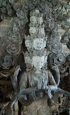 an intricately carved statue in front of a wall with many heads and arms on it