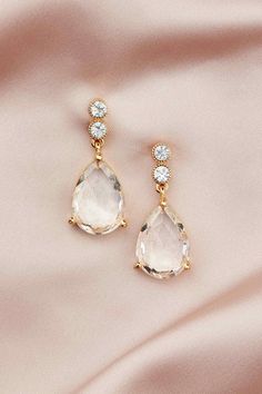 two pairs of gold earrings with white stones on pink silk background, close up view