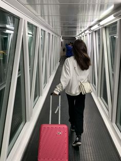 a woman walking down a hallway with a pink suitcase