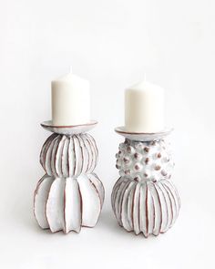 two white candles sitting on top of each other next to each other in front of a white background