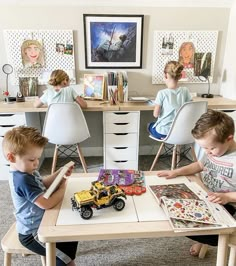 three children are sitting at a table with toys in front of them and one boy is reading