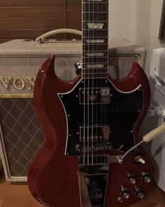 a red electric guitar sitting on top of a wooden floor