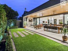 an outdoor living room and dining area are lit up at night, with grass in the foreground