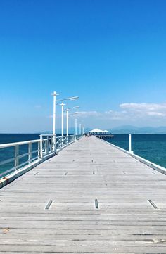 a long pier stretching out into the ocean on a sunny day with blue sky and water in the background