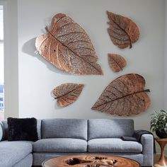 a living room with a couch, table and three metal leaf wall art pieces on the wall