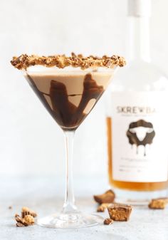 a chocolate martini in a glass next to a bottle of booze and walnuts