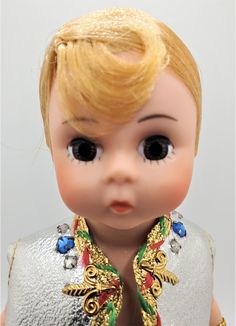 a close up of a doll wearing a silver dress with gold and red accents on it's chest