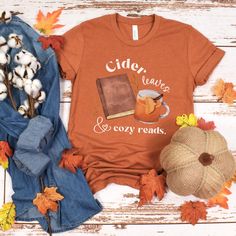 Get cozy this season with our fall reading shirt! Featuring the phrase "Cider, leaves, and cozy reads," this cute book lover shirt is perfect for autumn days spent with a good book and a warm cider. Whether you're a librarian or just love the fall vibes, this fall apple cider shirt is a must-have for your seasonal wardrobe. Embrace the autumn spirit with this stylish and bookish shirt that's perfect for any reader! STYLE + SIZING ★ UNISEX Bella+Canvas 3001 T-Shirt ★ Colors may vary (see photo card for more info). ★ See photos for a size chart specific to this t-shirt style. ★ Measuring Tip: Lay your favorite t-shirt on a flat surface, then measure width (armpit to armpit) and length (top to bottom) to compare with our size chart. ★ Styled for photos - any props are NOT included with purcha Fall Bookish Tops With Graphic Print, Fall Graphic Print Bookish Tops, Cozy Graphic Print T-shirt For Fall, Bookish Fall T-shirt With Letter Print, Fall Slogan T-shirt With Relaxed Fit, Fall Bookish T-shirt With Letter Print, Fall Themed T-shirt With Character Print, Fall Apple Cider, Fall Sublimation Print Relaxed T-shirt