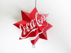 a red and white origami star hanging from a hook with the word coca - cola on it