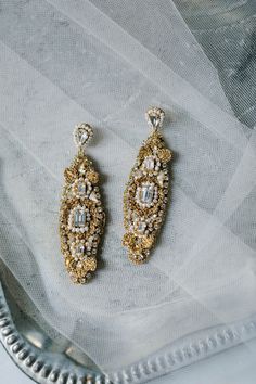 two pairs of earrings sitting on top of a white cloth covered table next to a silver tray