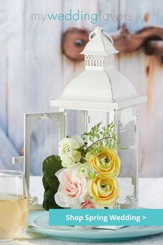 a table topped with a vase filled with flowers next to a glass of white wine