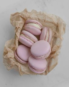 a bunch of pink macaroons sitting in a paper bag on a marble surface