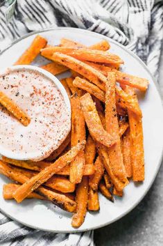 a white plate topped with french fries covered in ranch dressing next to a bowl of dip