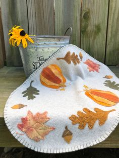 an autumn table cloth with leaves and acorns on it next to a flower pot