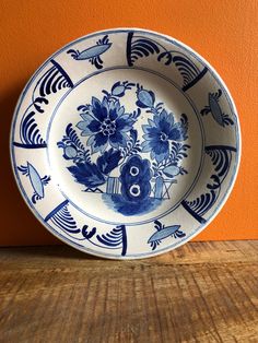 a blue and white plate sitting on top of a wooden table next to an orange wall