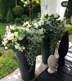 three black vases filled with white flowers and greenery on a wooden table outside