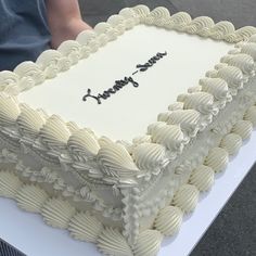 a large white sheet cake sitting on top of a table next to a persons hand