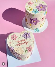 two decorated heart shaped cakes sitting on top of a pink table cloth covered in white frosting