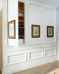 an empty room with white paneling and framed pictures on the wall, along with bookshelves