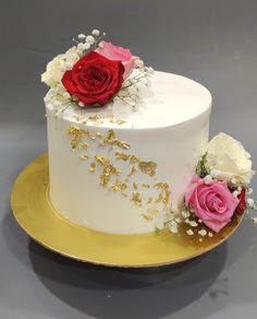 a white cake with red and pink roses on top is sitting on a gold plate