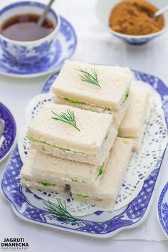 there are four sandwiches on the plate and two cups of tea in the bowl next to them