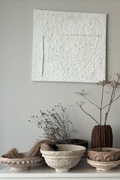 three white vases with plants in them on a shelf next to a wall hanging