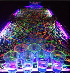 several shot glasses are lined up in front of a neon light display on a table