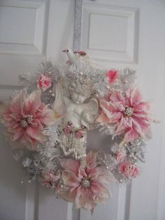 a wreath with pink and white flowers hanging on the front door is adorned with an angel figurine