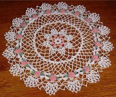 a white doily with pink and green flowers on it sitting on a wooden table