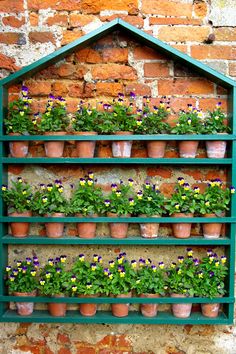 a green shelf filled with potted plants next to a brick wall