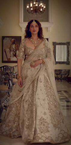 a woman in a white and gold wedding gown standing next to a chandelier