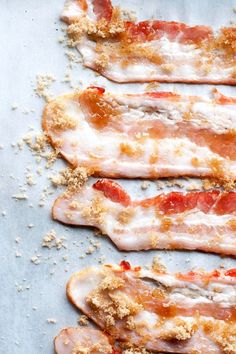 bacon strips covered in cheese and seasoning on a sheet of baking paper with sprinkles