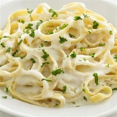 a plate filled with pasta covered in white sauce and parsley on top of it