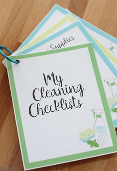 four cleaning checklist cards sitting on top of a wooden table with blue and green trimming