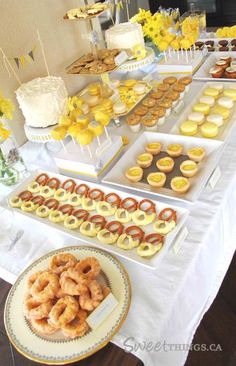 an assortment of pastries and desserts displayed on a long table with yellow flowers