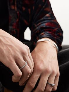 a man sitting on the floor with his hands clasped together, wearing two different rings